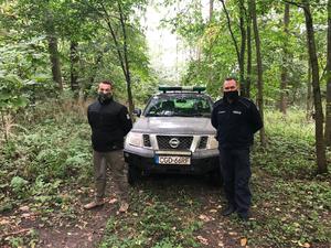 policjant i strażnik leśny stoją przy samochodzie w lesie