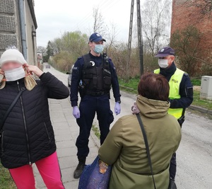 dwóch umundurowanych policjantów stoi na chodniku twarzą do kobiety, w tle widać radiowóz poolicyjny