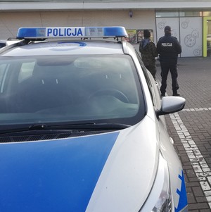 Na zdjęciu policjant i żołnierz stojący przed wejściem do marketu.