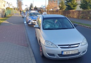 fotografia auta z rozbitą szybą czołową w tle radiowóz policji, fotografie z miejsca wypadku drogowego, srebrne auto przewrócone w przydrożnym rowie