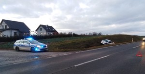 fotografia auta z rozbitą szybą czołową w tle radiowóz policji, fotografie z miejsca wypadku drogowego, srebrne auto przewrócone w przydrożnym rowie