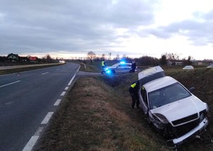 fotografia auta z rozbitą szybą czołową w tle radiowóz policji, fotografie z miejsca wypadku drogowego, srebrne auto przewrócone w przydrożnym rowie