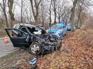 Samochód osobowy po wypadku. Całkowicie zniszczony przód, obok zaparkowany oznakowany radiowóz policji.