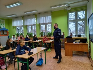 Policjant w klasie, dzieci w ławkach, funkcjonariusz stoi przed nimi, przedstawia prezentację multimedialną