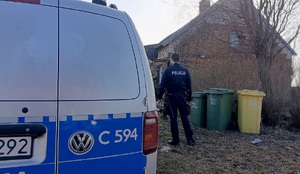 oznakowany radiowóz stoi przed domem, a obok stoi policjant